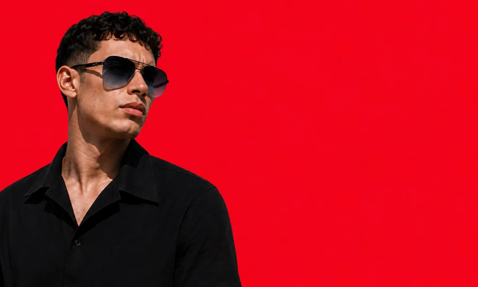 Man wearing angular black sunglasses beside a Numyra monogram pattern
